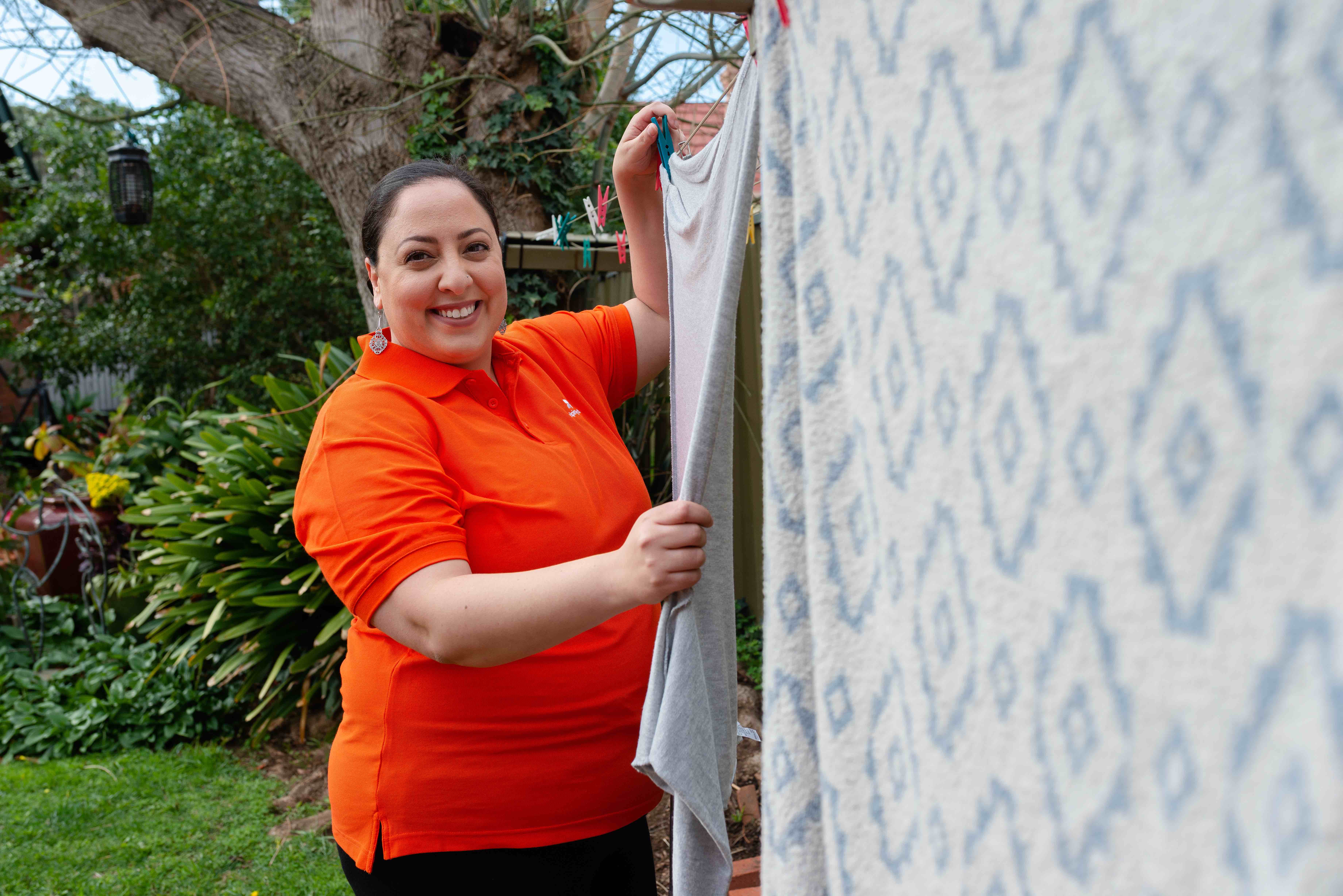 female home care worker in bright orange shirt hangs a patterned towel on the clothes line.