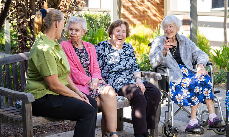 Elderly women sitting outside on bench chatting